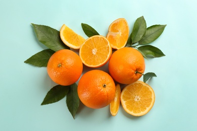 Photo of Fresh ripe oranges with green leaves on light blue background, flat lay
