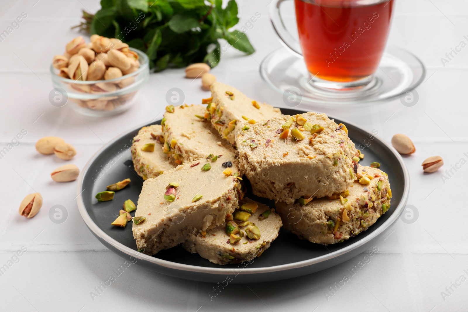 Photo of Tasty halva with pistachios served on white tiled table, closeup