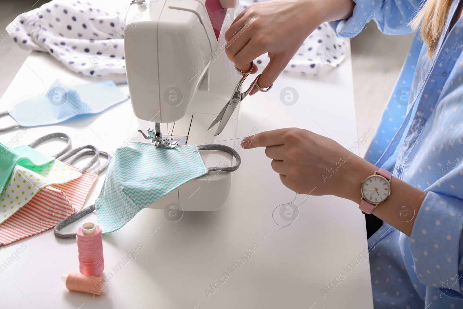 Photo of Woman making cloth mask with sewing machine at white table, closeup