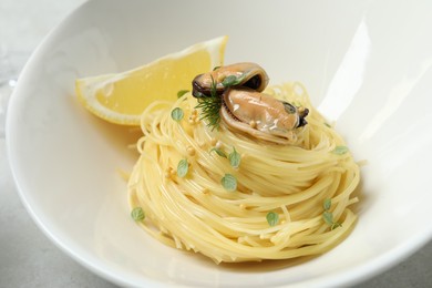 Photo of Tasty capellini with mussels and lemon on plate, closeup. Exquisite presentation of pasta dish