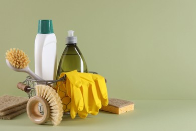 Set of different cleaning supplies in basket on light green background. Space for text