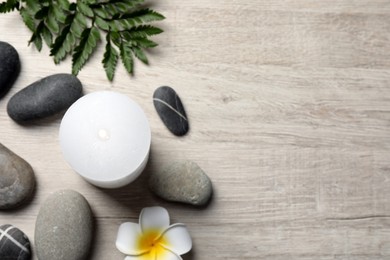 Photo of Burning candle, plumeria flower and spa stones on light beige wooden table, flat lay. Space for text