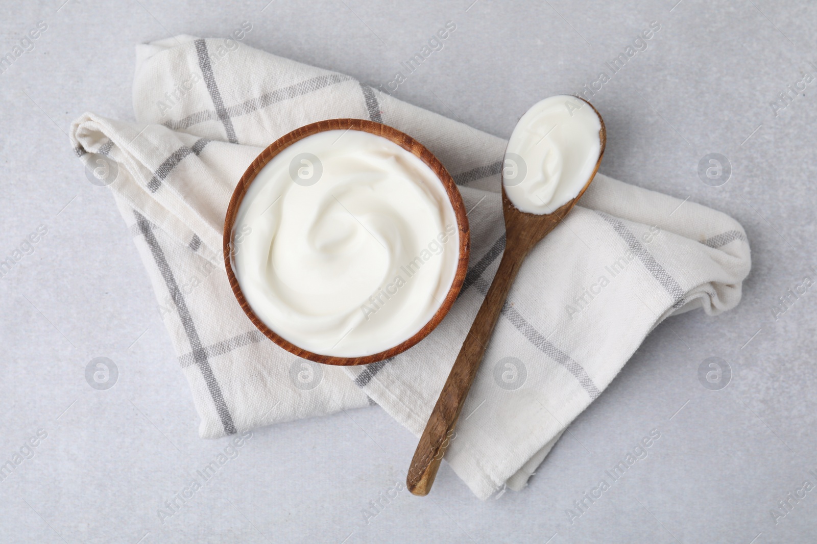 Photo of Delicious natural yogurt in bowl and spoon on light grey table, top view