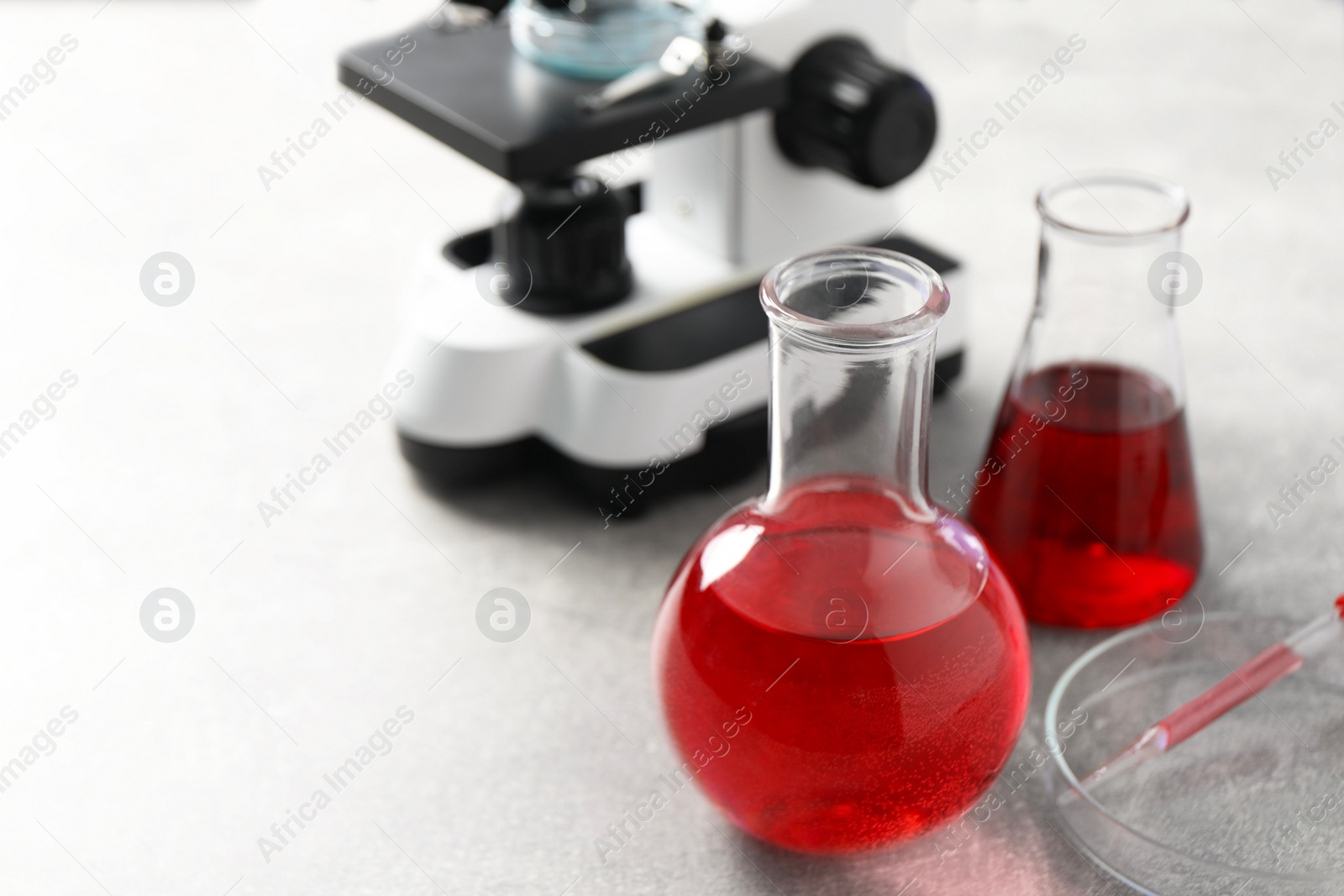 Photo of Laboratory analysis. Flasks with red liquid, petri dish and microscope on light grey table