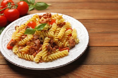 Plate of delicious pasta with minced meat, tomatoes and basil on wooden table, closeup