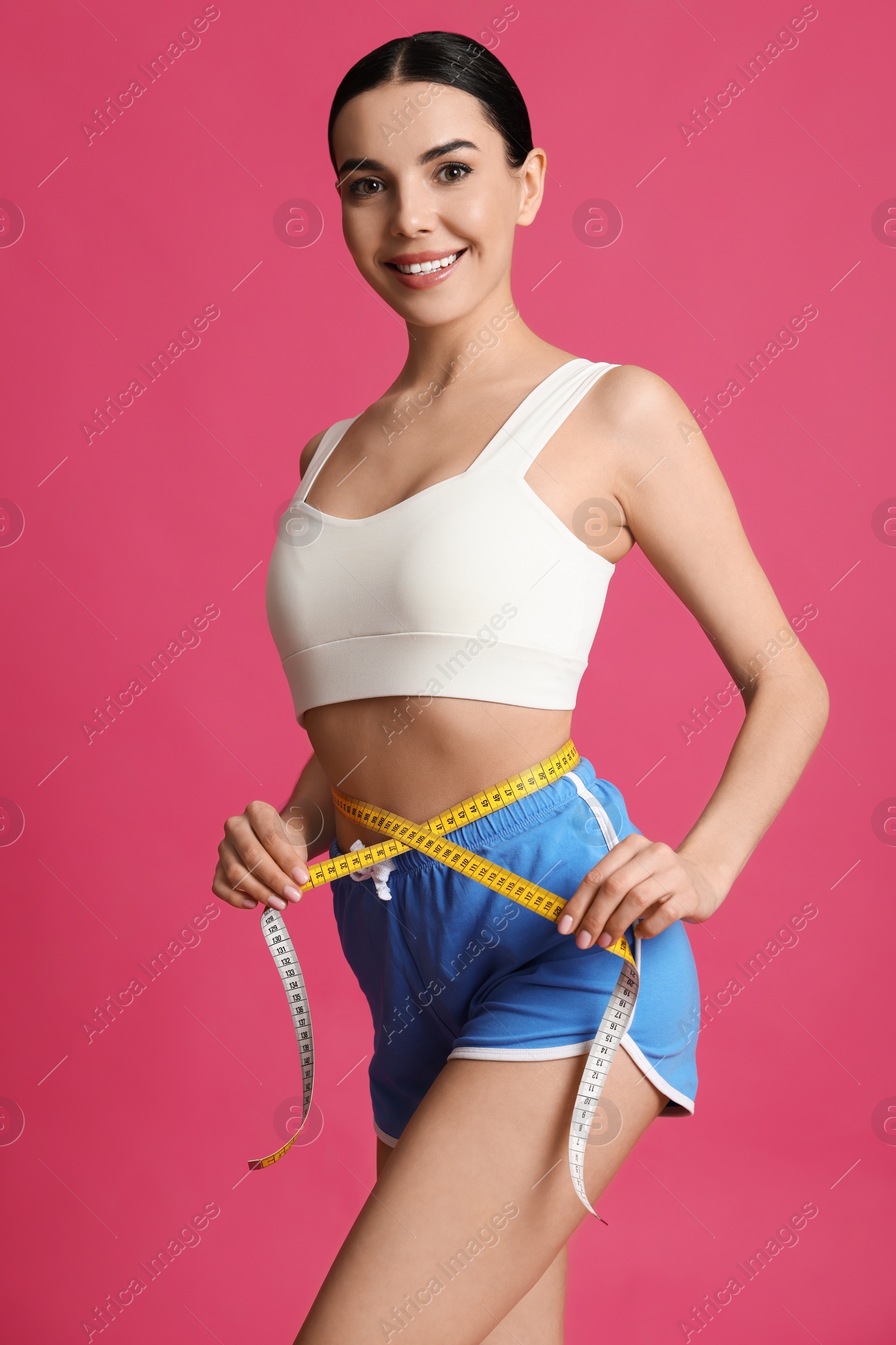 Photo of Young woman measuring waist with tape on pink background