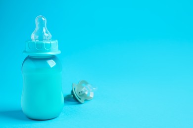 One feeding bottle with milk and pacifier on light blue background. Space for text