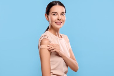 Photo of Woman with sticking plaster on arm after vaccination against light blue background