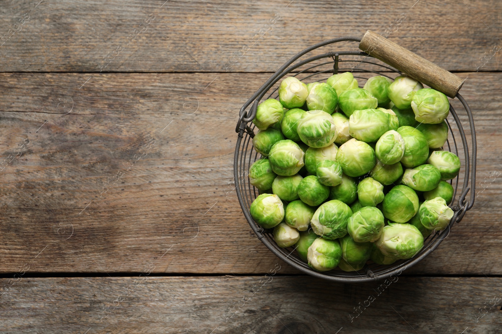 Photo of Metal basket with fresh Brussels sprouts on wooden background, top view. Space for text