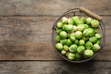 Photo of Metal basket with fresh Brussels sprouts on wooden background, top view. Space for text