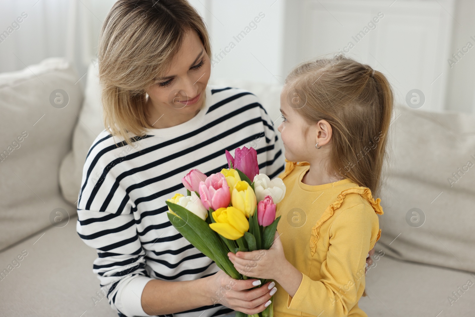 Photo of Little daughter congratulating her mom with bouquet of beautiful tulips at home. Happy Mother's Day