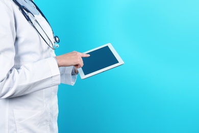 Female doctor holding modern tablet on color background, closeup with space for text