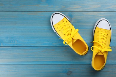 Photo of Pair of yellow sneakers on light blue wooden table, flat lay. Space for text