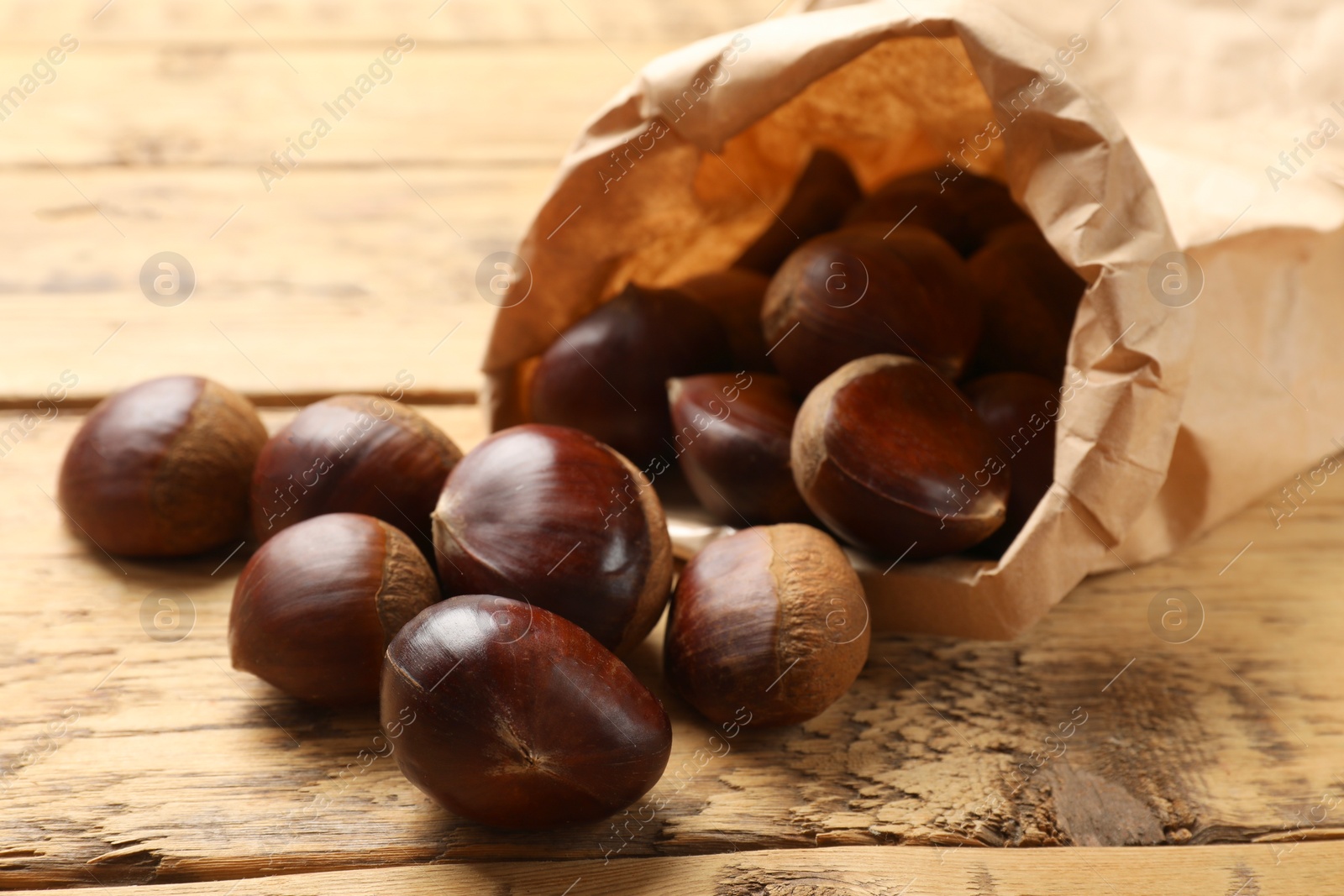 Photo of Sweet fresh edible chestnuts in paper bag on wooden table, closeup
