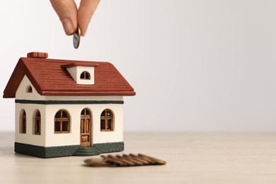 Photo of Mortgage concept. Woman putting coin into house model at wooden table against white background, closeup with space for text