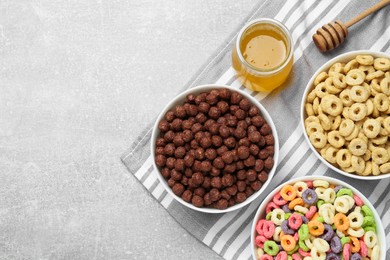 Different delicious breakfast cereals and honey on light grey table, flat lay. Space for text