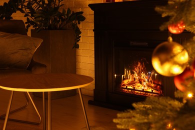 Photo of Christmas tree with baubles near cosy fireplace indoors
