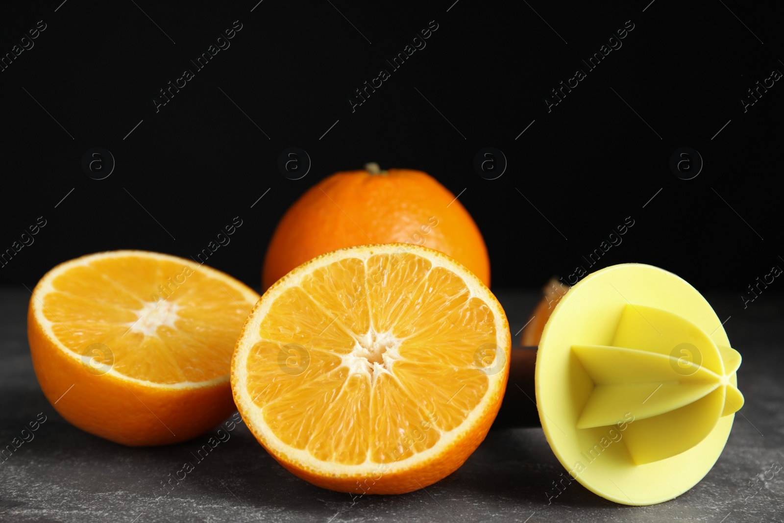 Photo of Fresh ripe oranges and reamer on grey table, closeup