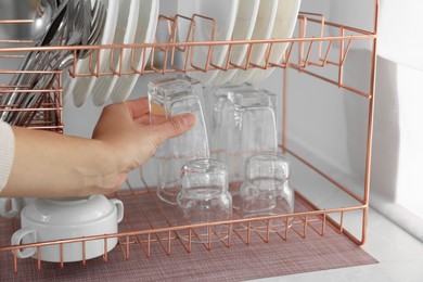 Photo of Woman putting clean glass on dish drying rack in kitchen, closeup