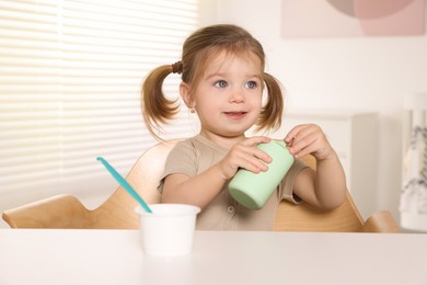 Photo of Cute little child with bottle and cup of tasty yogurt at white table indoors