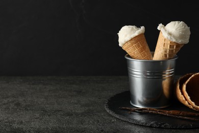 Photo of Ice cream scoops in wafer cones on gray textured table against dark background, space for text