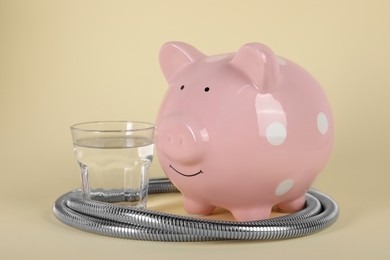 Water scarcity concept. Piggy bank, shower hose and glass of drink on beige background