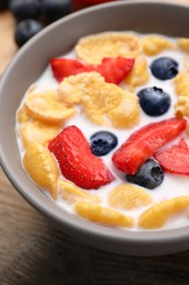 Photo of Bowl of tasty crispy corn flakes with milk and berries on wooden table, closeup