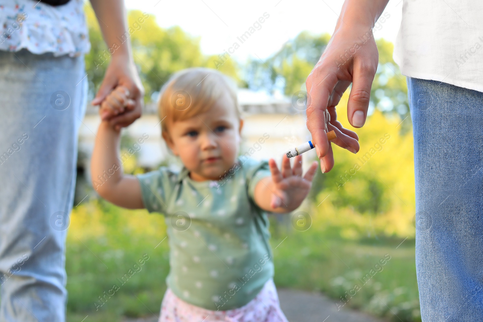 Photo of Woman smoking cigarette in public place outdoors, closeup. Don't smoke near kids