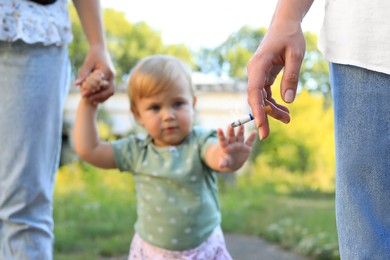 Photo of Woman smoking cigarette in public place outdoors, closeup. Don't smoke near kids