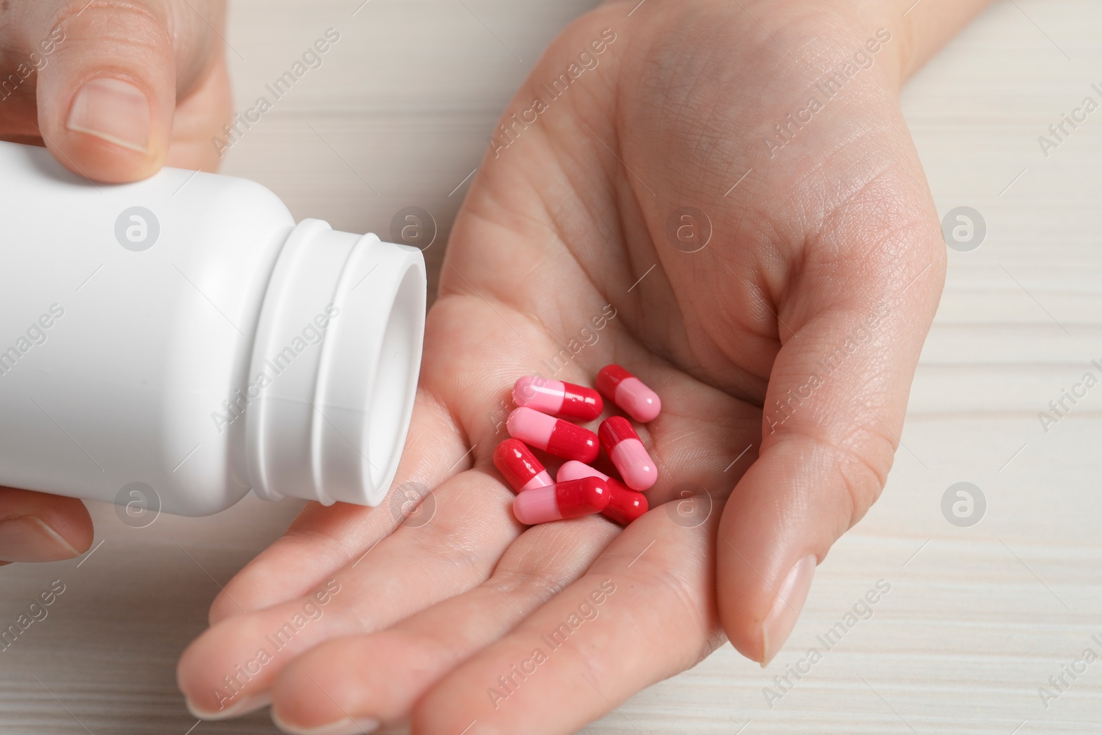 Photo of Woman pouring pills from bottle onto hand at white wooden table, closeup