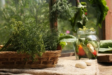Photo of Fresh green herbs, jar with tomatoes and garlic cloves on wooden table indoors