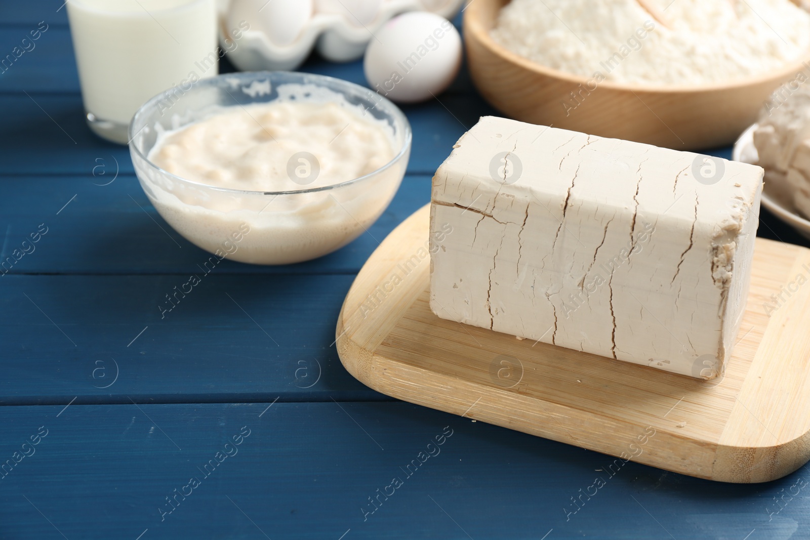 Photo of Block of compressed yeast near dough ingredients on blue wooden table