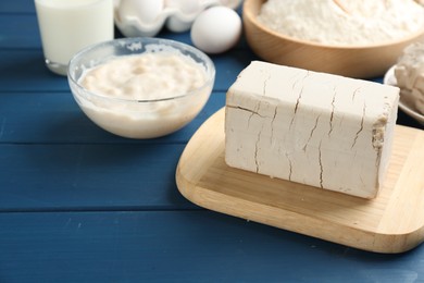 Block of compressed yeast near dough ingredients on blue wooden table