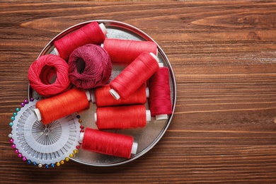 Photo of Color sewing threads and pins on wooden background, top view