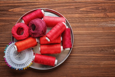 Color sewing threads and pins on wooden background, top view