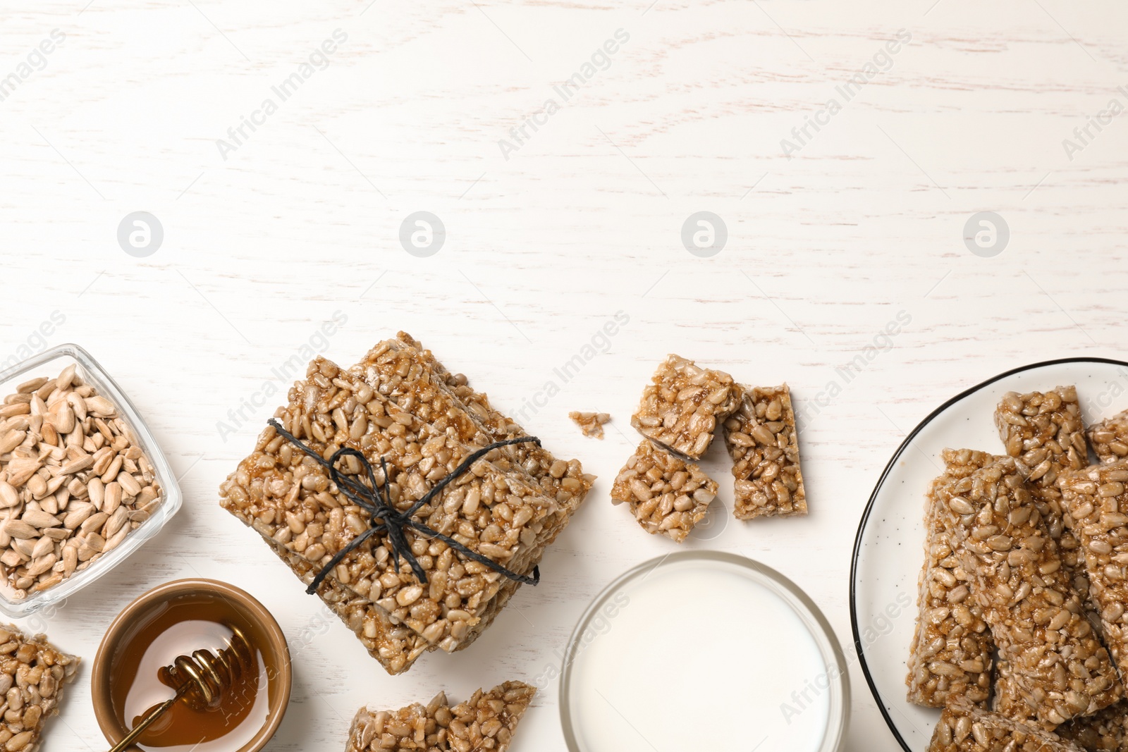 Photo of Delicious sweet kozinaki bars, honey and milk on white wooden table, flat lay. Space for text