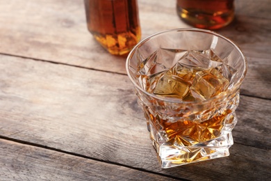 Photo of Golden whiskey in glass with ice cubes on table. Space for text