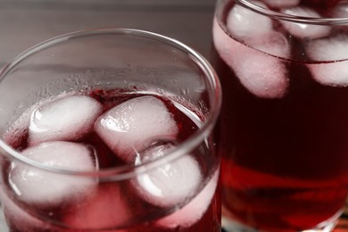 Refreshing hibiscus tea with ice cubes in glasses on table, closeup