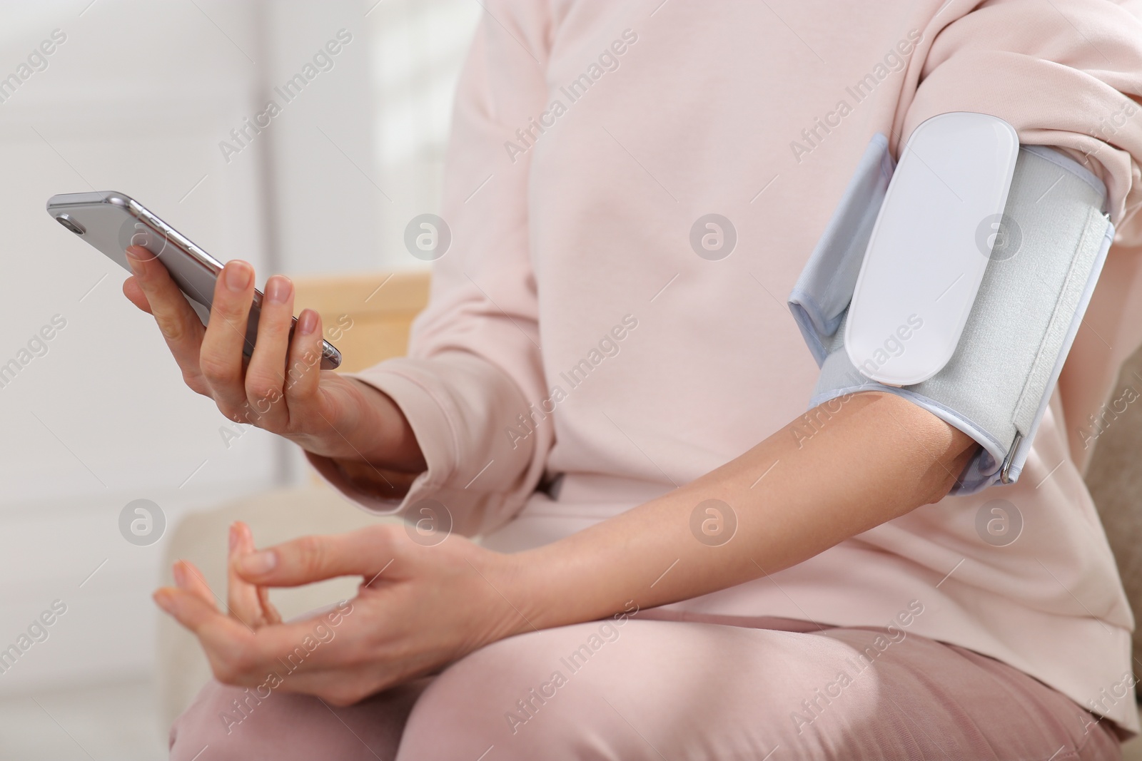 Photo of Woman checking blood pressure with modern monitor and smartphone indoors, closeup