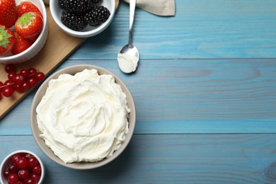 Photo of Tasty cream cheese and fresh berries on light blue wooden table, flat lay. Space for text