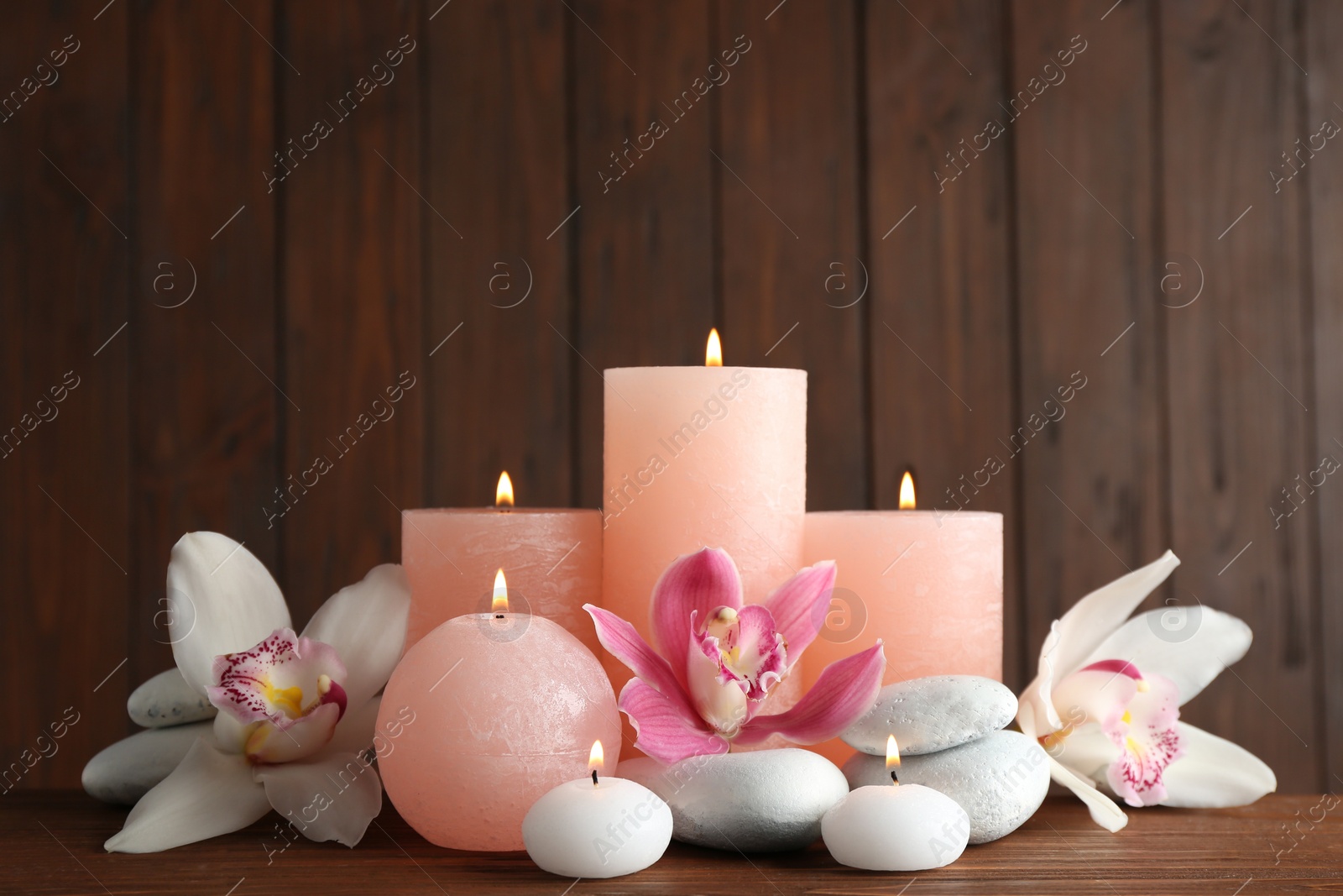 Photo of Beautiful composition with candles, flowers and stones on table against wooden background