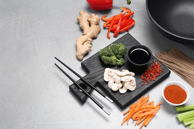 Photo of Wok, chopsticks and different products on grey table, space for text