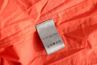 Clothing label in different languages on orange garment, closeup