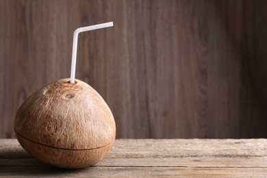 Coconut water. Fresh nut with straw on wooden table, space for text