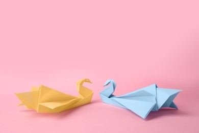 Photo of Origami art. Beautiful paper swans on pink background