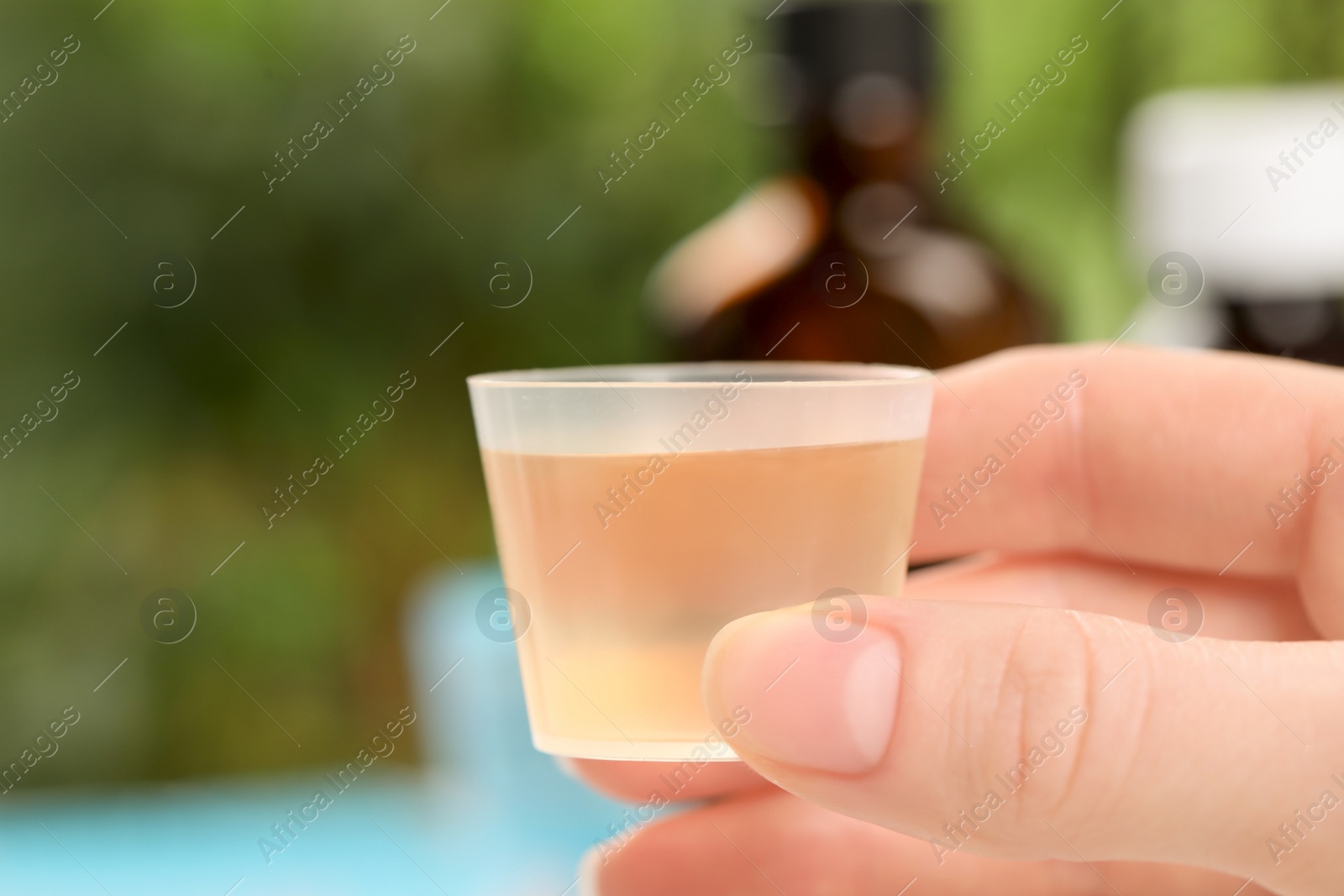 Photo of Woman holding measuring cup with syrup on blurred background, closeup. Cold medicine