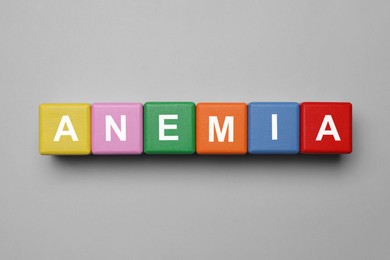 Photo of Wooden cubes with word Anemia on grey background, flat lay
