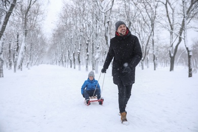 Father sledding his child outside on winter day. Christmas vacation