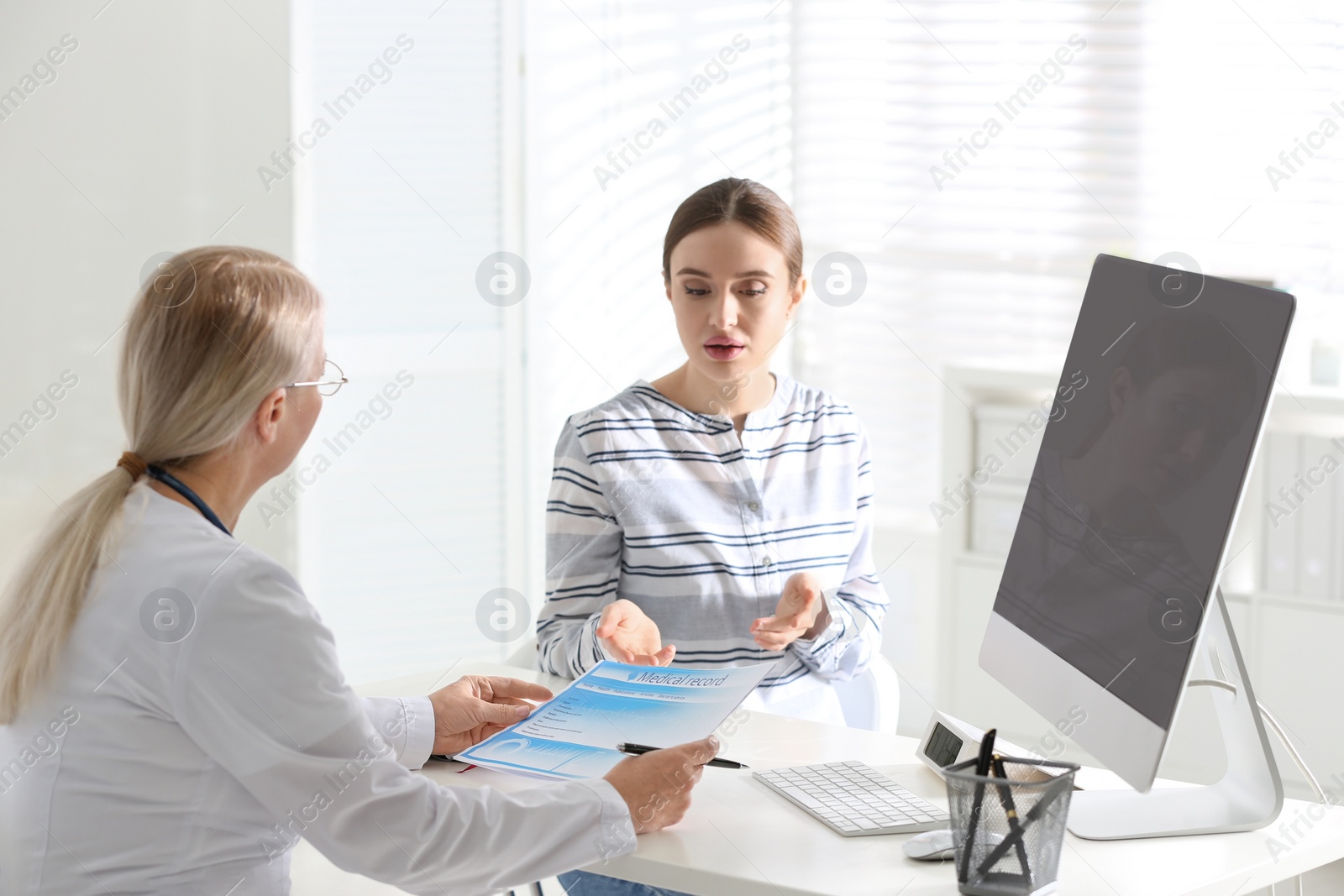 Photo of Doctor consulting patient at desk in clinic