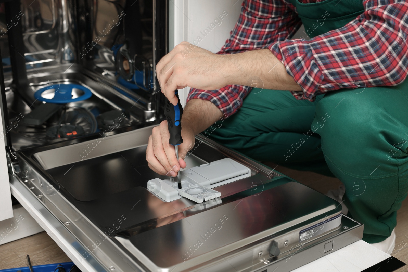 Photo of Serviceman repairing dishwasher with screwdriver indoors, closeup